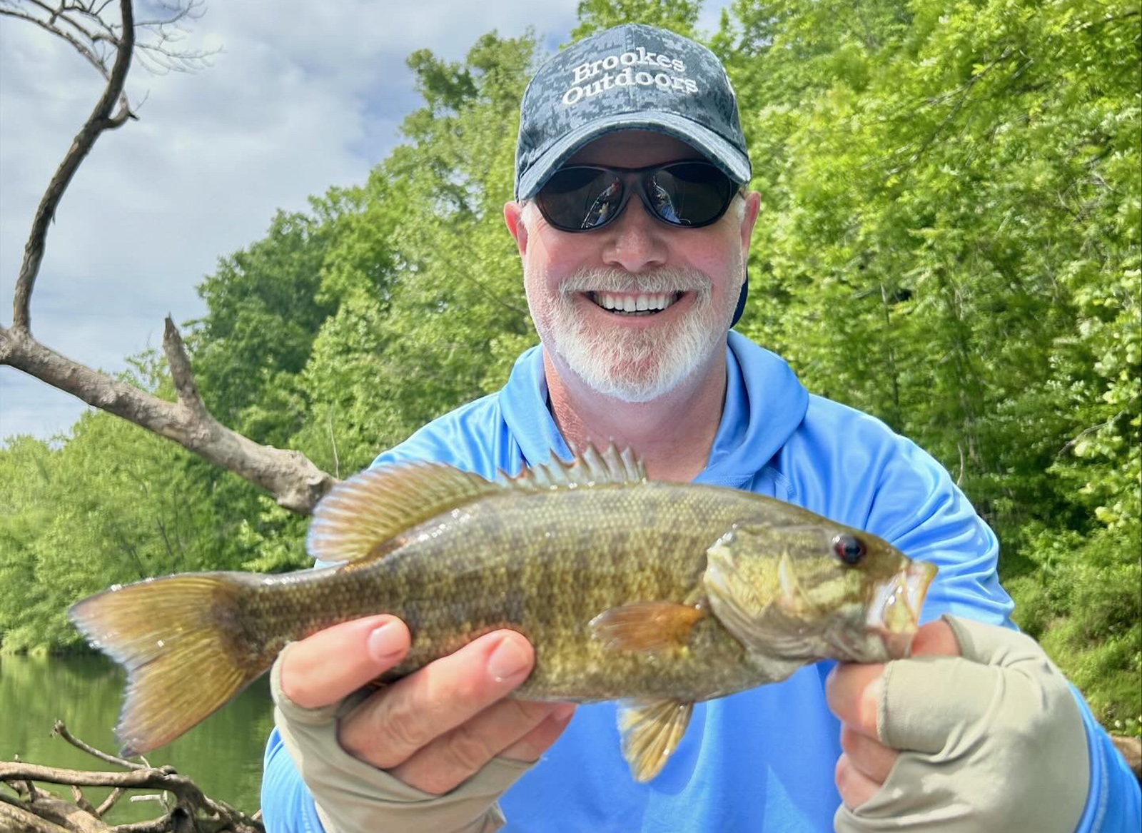 A man holding a smallmouth bass fish for a photo.